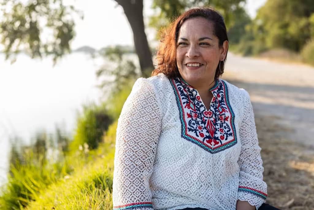Une Mexicaine portant un chemisier blanc est assise près d'un plan d'eau.